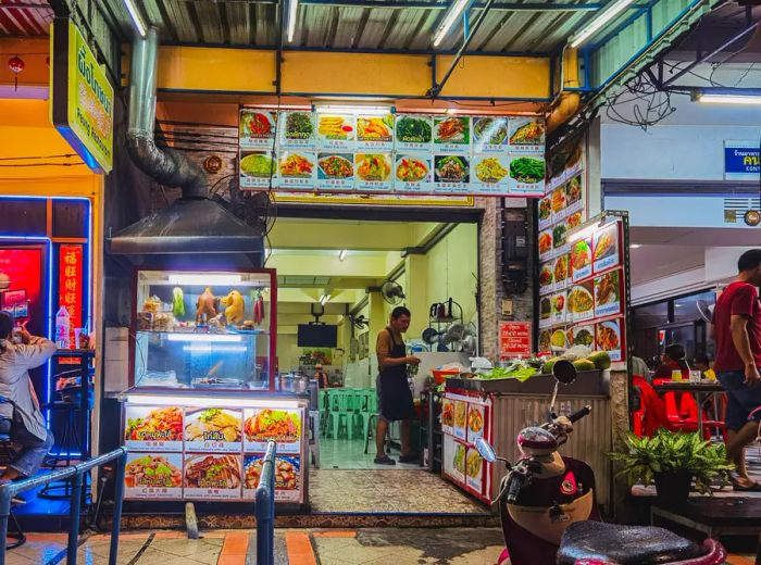 In front of a narrow eatery situated within a food hall.