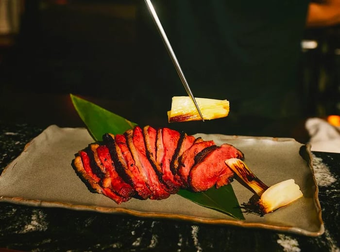 A chef artfully presents a root vegetable next to sliced duck breast.