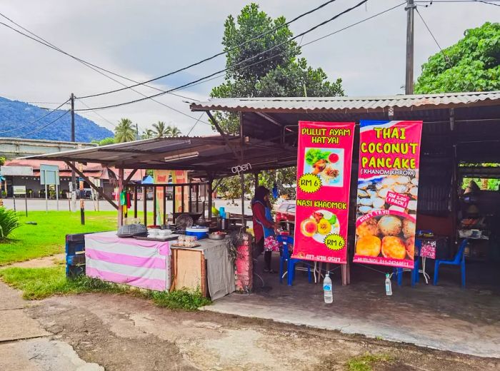 A roadside stand showcasing a variety of dishes in both Thai and English.