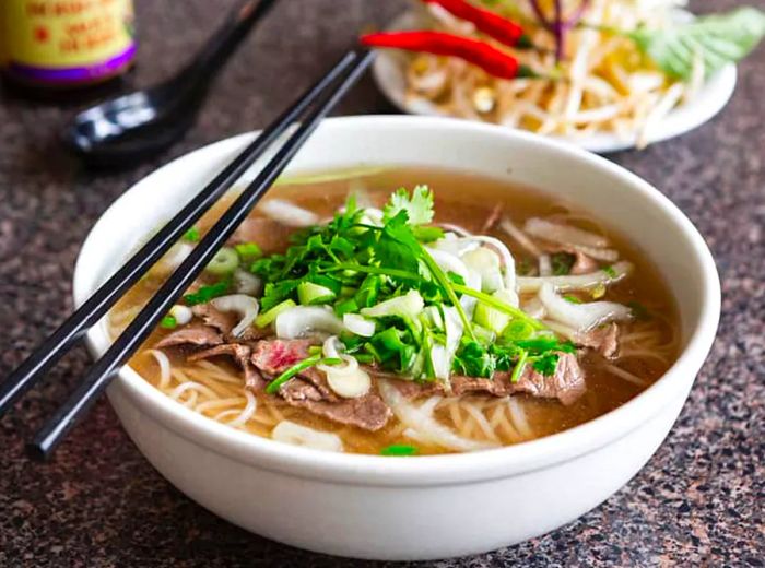 A bowl of pho garnished with fresh herbs.