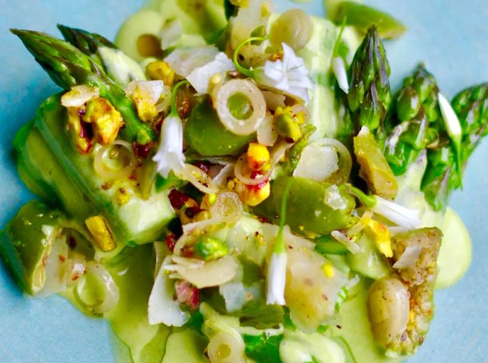 Chopped asparagus topped with a green sauce and adorned with layers of edible flowers and other garnishes.