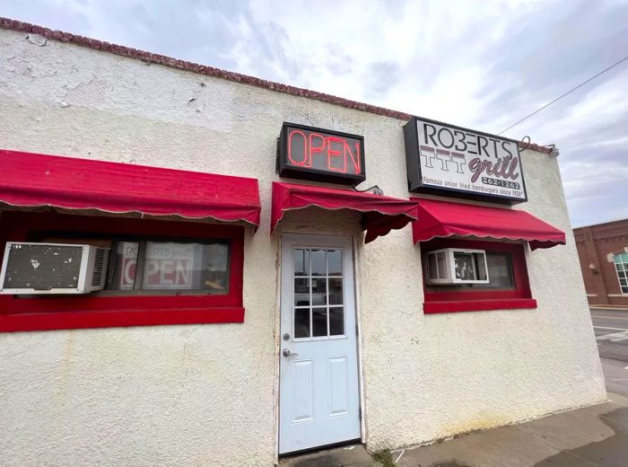 A modest building exterior featuring a neon 'open' sign along with other signage for Robert’s Grill.