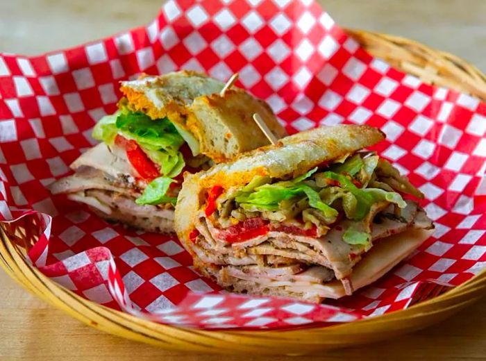 Two sandwich halves showcased in checkerboard paper, stacked high with sliced meats and fresh vegetables.