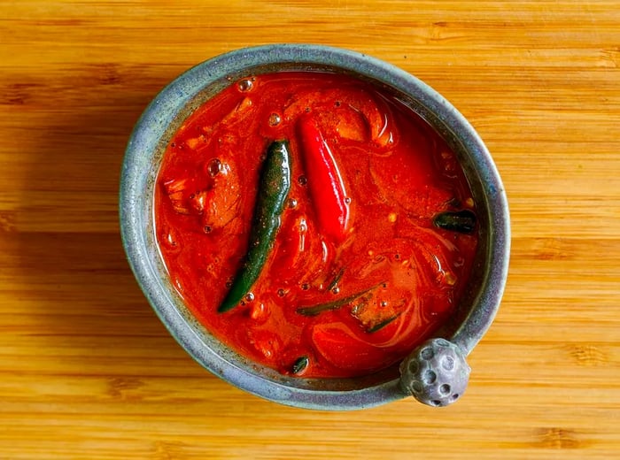 A top-down perspective of a bowl filled with a vibrant red sauce, with chiles floating inside.