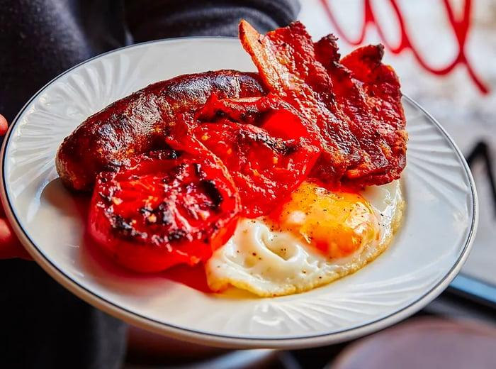 A plate featuring sausage, roasted tomatoes, and fried eggs.