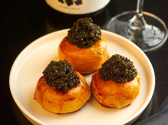 A plate with three knishes topped with caviar, accompanied by a bottle of wine.