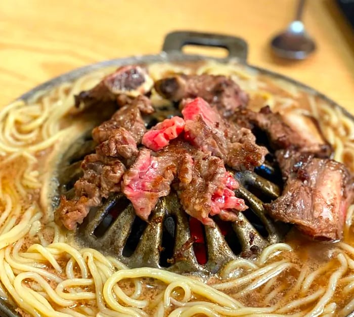 Grilled beef slices resting on a grill, encircled by steaming noodles.