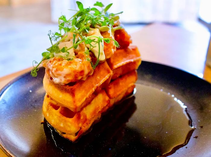 A double stack of waffles topped with glazed shrimp and greens.