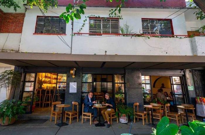 Patrons enjoy their meals at outdoor tables in front of a restaurant, nestled within a residential-style building.