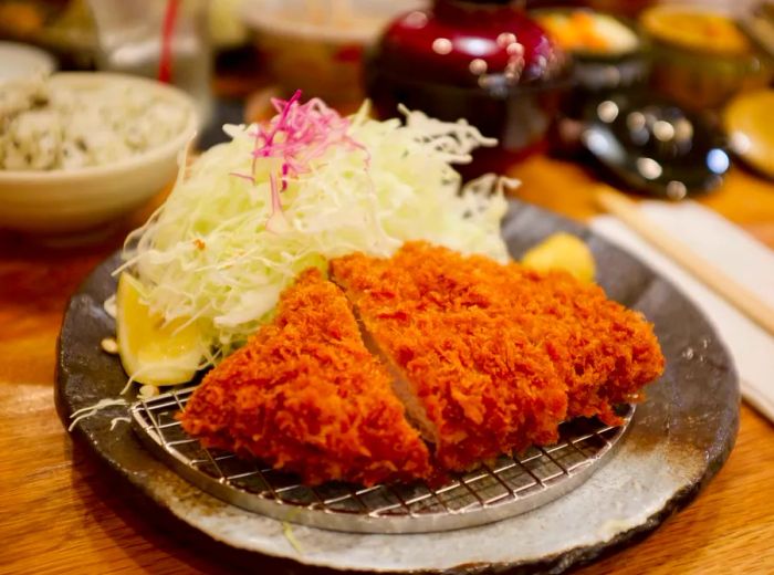 Sliced pork katsu resting on a metal grate, accompanied by a mound of cabbage.