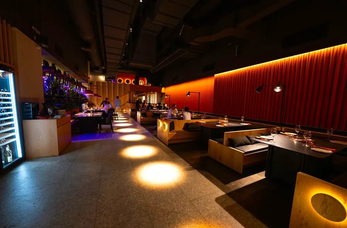 A spacious, dimly lit dining area featuring spotlights, where guests relax in low wooden booths.