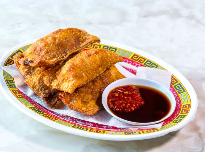 A decorative plate holding fried dumplings accompanied by a dipping sauce.