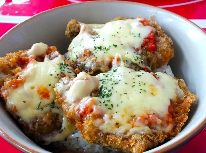 Three sizable pieces of fried meat, topped with cheese and tomatoes, served on a bed of rice.