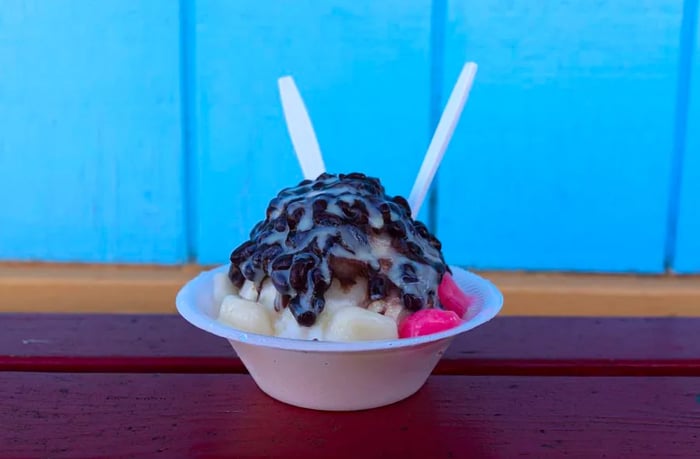 A plastic cup filled with shaved ice, generously drizzled with chocolate topping.