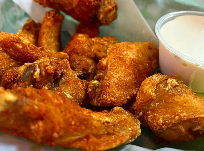 Crispy fried chicken wings served in a paper-lined basket with a side of dipping sauce.