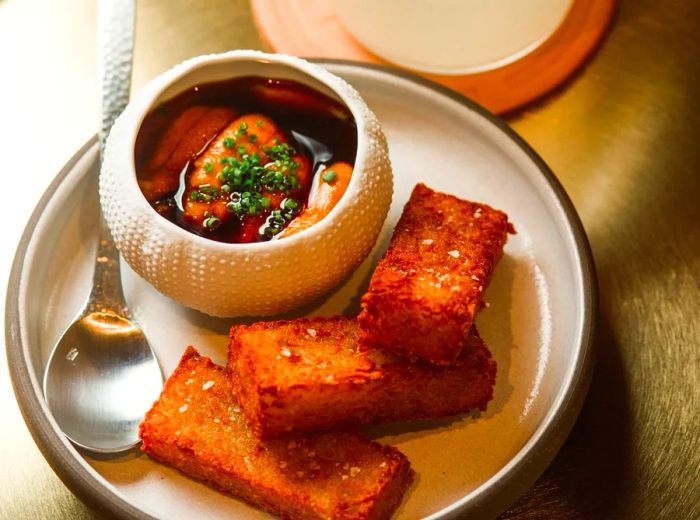 A plate of rectangular potato croquettes, accompanied by a small bowl of uni and a white cocktail.