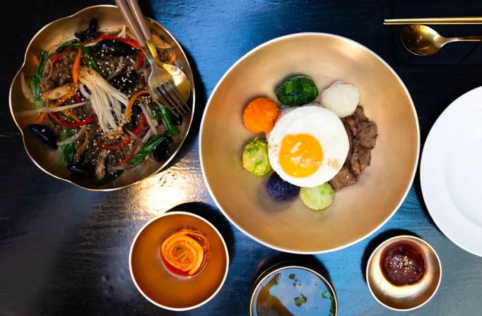 An overhead view showcases beautifully plated bibimbap accompanied by side dishes and a noodle dish.