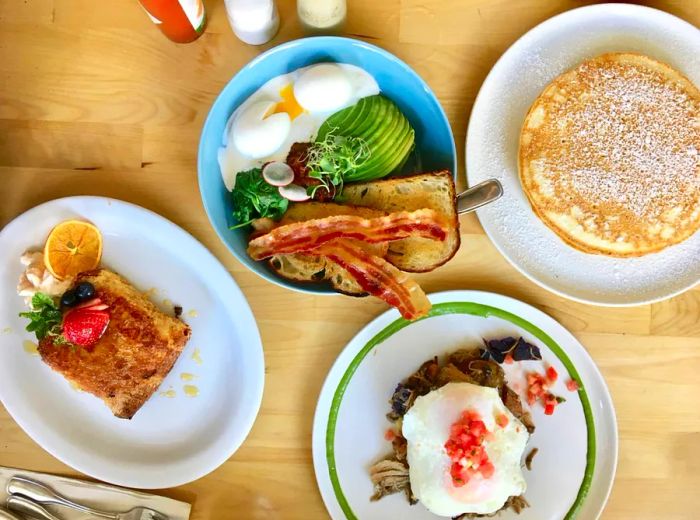 An aerial view of a table featuring pancakes, a bacon-topped breakfast bowl, and various other dishes.