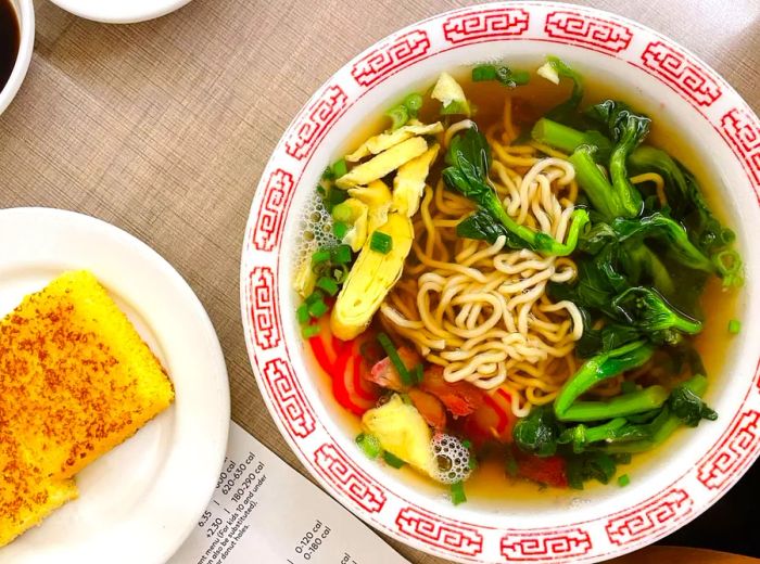 A steaming bowl of noodles in broth, topped with fresh vegetables.