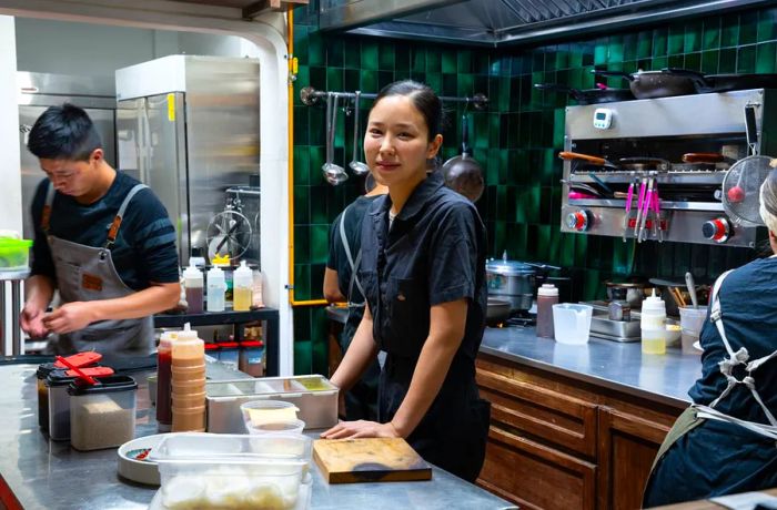 A chef gazes at the camera while others bustle around in the kitchen behind him.