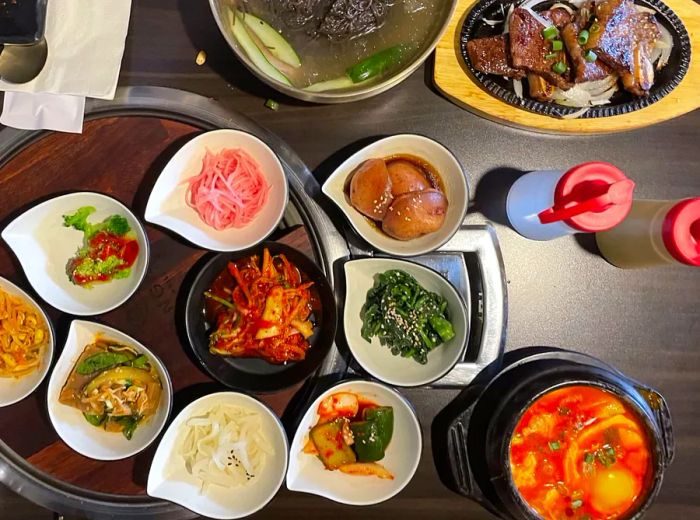 An array of banchan accompanied by a vibrant stew and grilled meats.