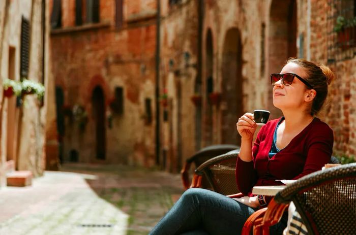 A young woman enjoying coffee at a café in a medieval Tuscan town, Italy