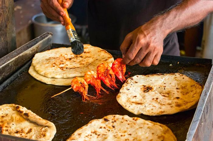 A Sri Lankan chef preparing prawns alongside pol roti flatbread in Colombo