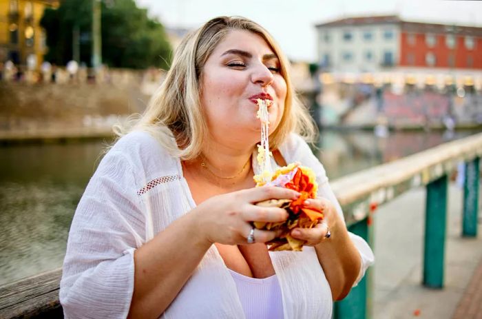 A close-up of a woman savoring arancini outdoors in Italy.