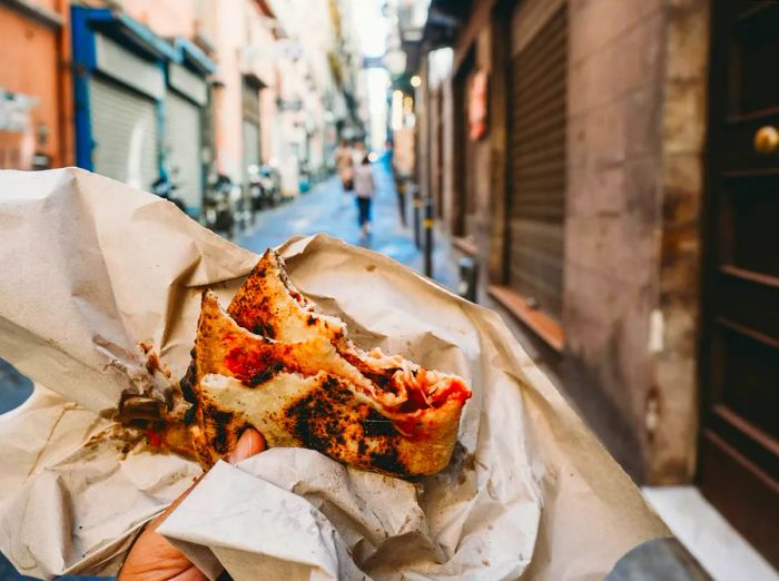 A point of view shot of a man enjoying a traditional 'Pizza a portafoglio' in Naples, Italy.