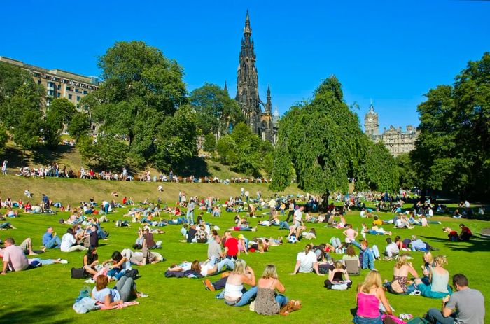 The Princes Street Gardens bustling with visitors, featuring the Scott Monument on a sunny summer day.