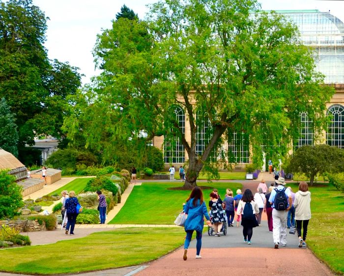 Visitors stroll towards the Victorian Palm House within the Royal Botanic Gardens of Edinburgh.