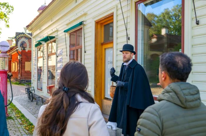 A guide in period attire leads visitors through historic structures at Skansen, an open-air museum in Stockholm.