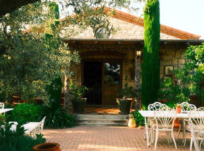 The exterior of a restaurant, adorned with white patio tables and lush greenery.