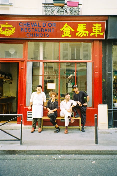 Four people enjoy their time outside a restaurant marked by a sign reading: Cheval d’Or Restaurant Chinois.