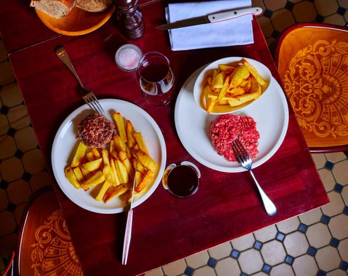 An aerial shot featuring steak tartare and a hamburger steak, both served with fries.