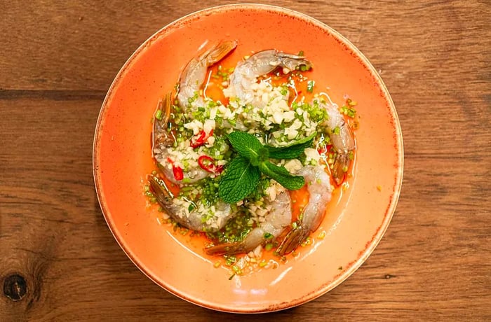 A bowl of shrimp garnished with chile sauce and mint, captured from above.