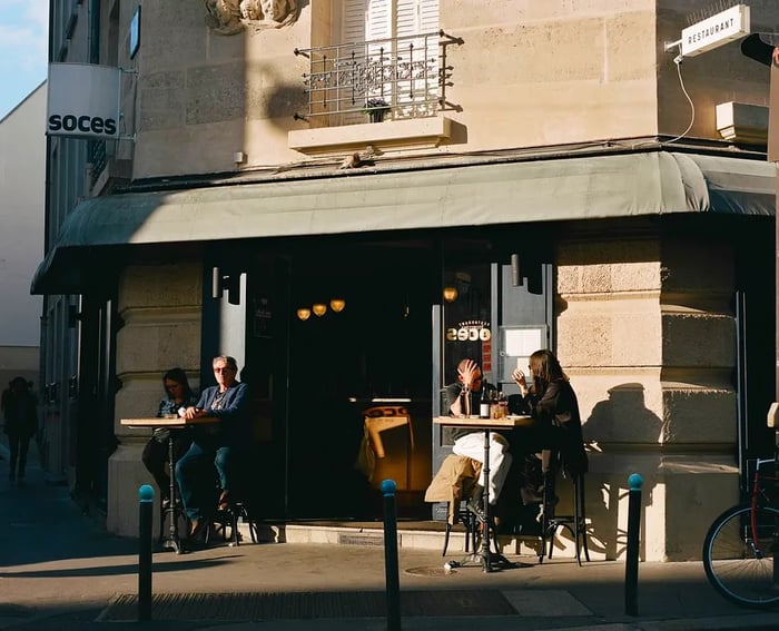 Diners enjoy outdoor seating at a corner restaurant on tall cafe tables