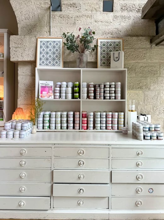 A white cabinet filled with numerous drawers, topped with stacks and shelves showcasing an array of jam jars.