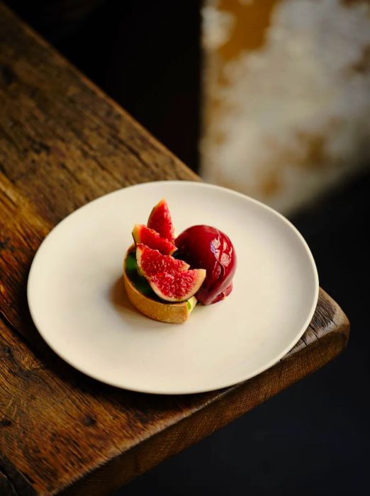 A half-cylinder tart adorned with fig slices next to a scoop of purple sorbet.