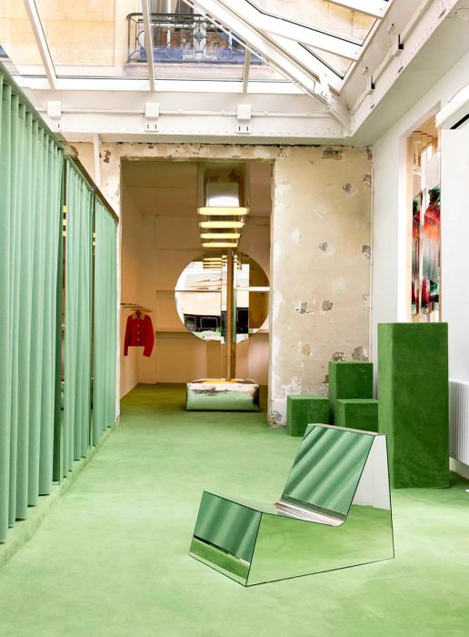 A fashion boutique featuring green carpets, stylish decorations, and changing room drapes, all beneath a spacious skylight.