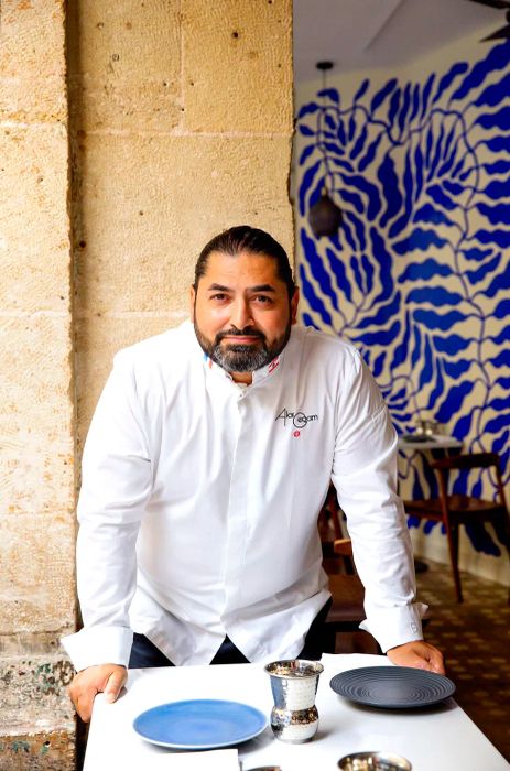 A chef leans over a dining table.