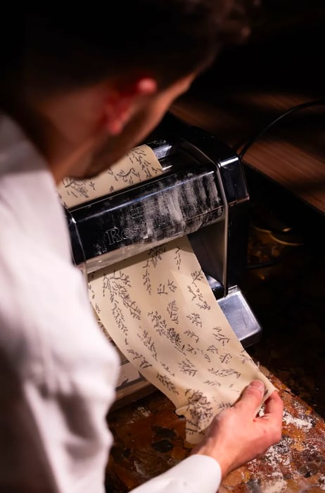 A chef skillfully presses patterned dough through a pasta machine.