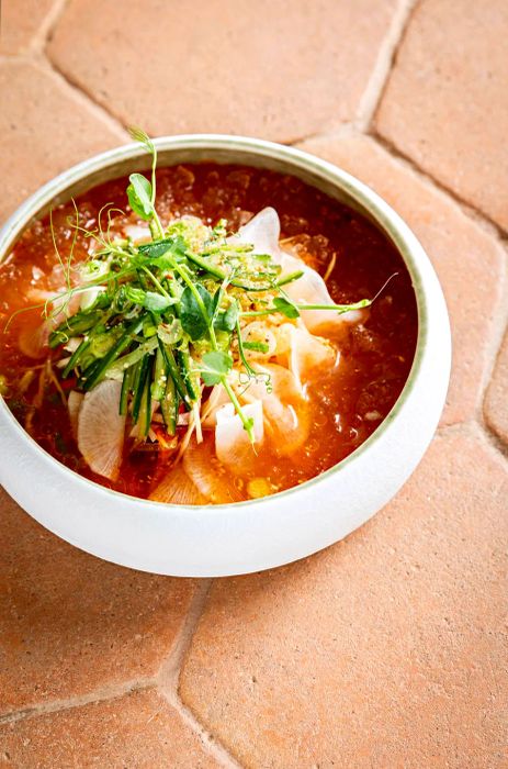 A bowl of mulhué featuring slices of fish and vegetables immersed in an orange ice bath.