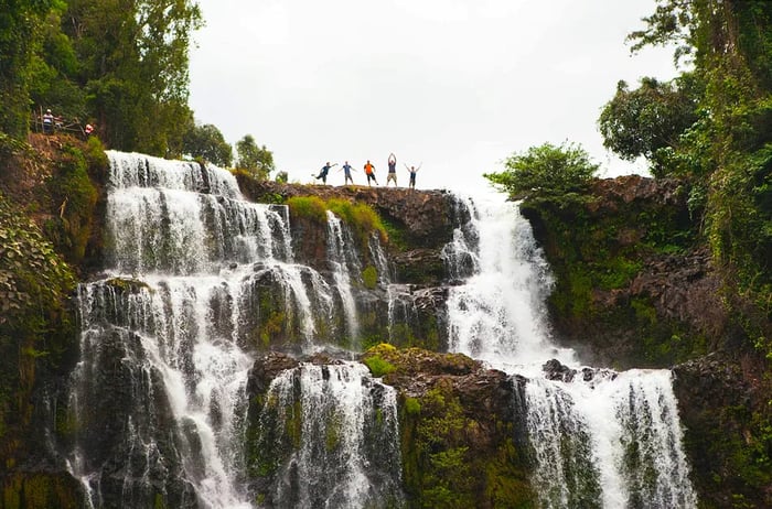 Five individuals pose triumphantly at the top of the magnificent Tad Yuang waterfalls on the Bolaven Plateau, Laos.