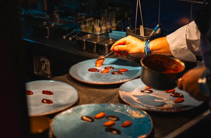 A chef drizzles various brown sauces onto elegant blue ceramic plates.