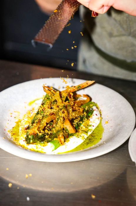 A chef delicately shaves bottarga over asparagus.