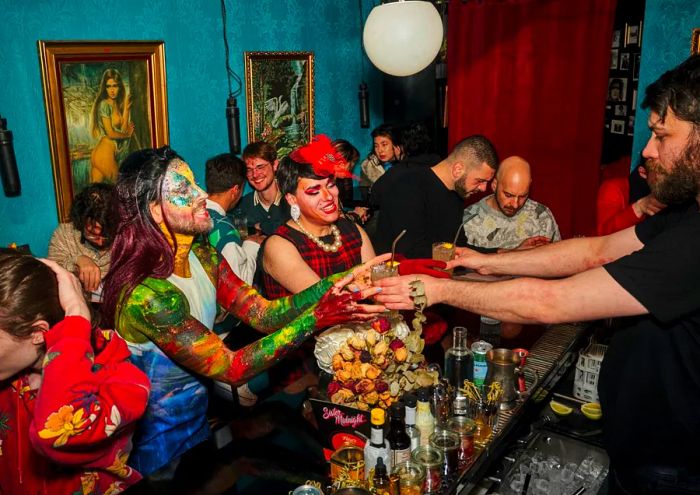 A bartender serves drinks to drag performers across the bar.