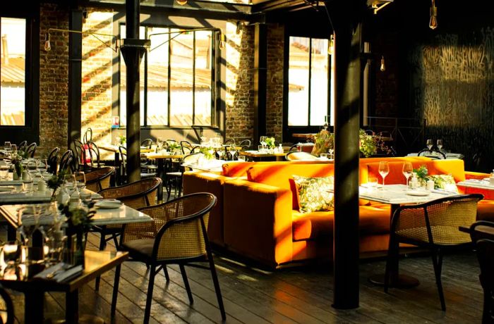 A restaurant dining area features a prominent orange couch, surrounded by exposed brick walls and imposing industrial columns.