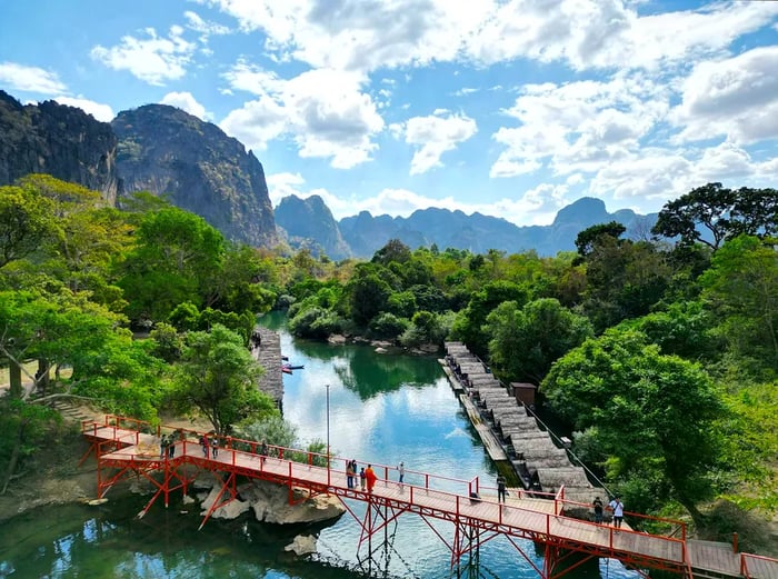 An aerial view captures a bridge spanning water near a breathtaking mountain range along the Tha Khaek Loop, Laos.