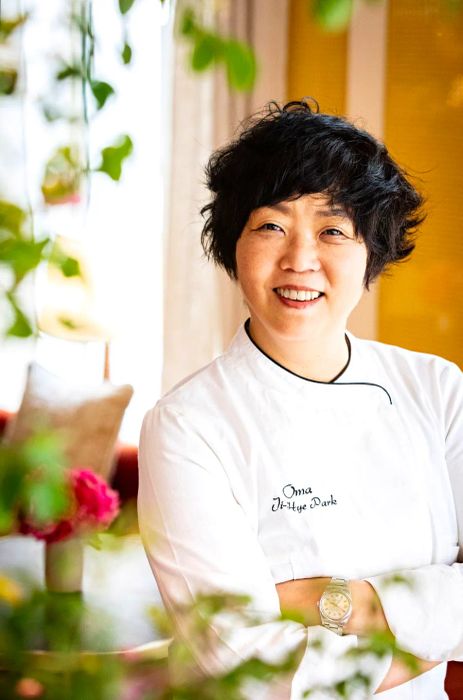 A chef stands with her arms crossed, dressed in her chef's whites.